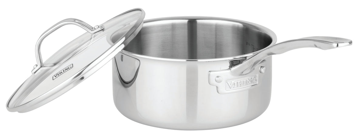 The Viking Culinary Products Artisan 3-ply Stainless Steel saucepan from the 11-piece set features a long handle and an open glass lid resting diagonally against the pot; it's induction compatible and oven safe.