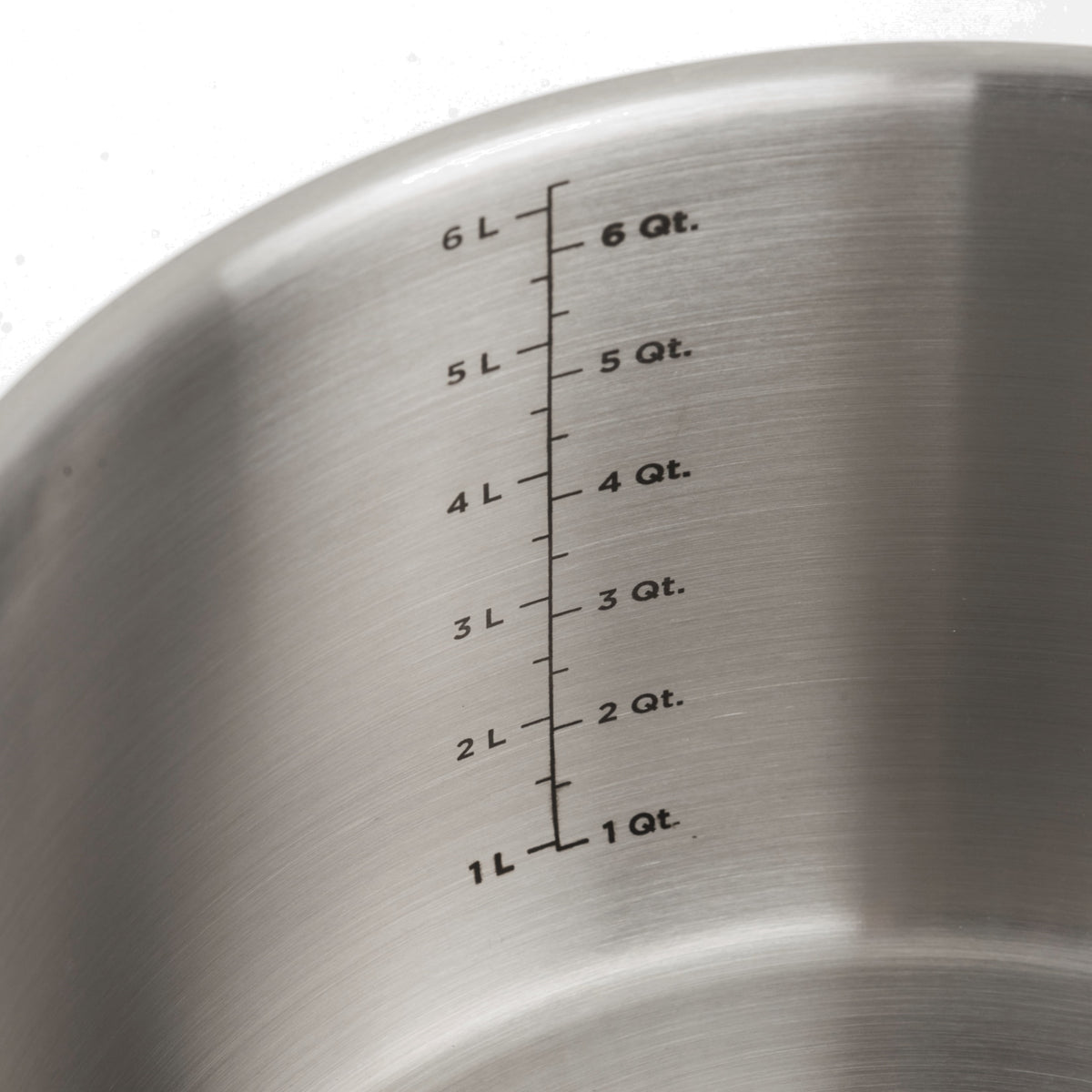 Close-up of the inside of a stainless steel pot, showing measurement markings in liters (1L to 6L) and quarts (1 Qt. to 6 Qt.) engraved on the metal surface.