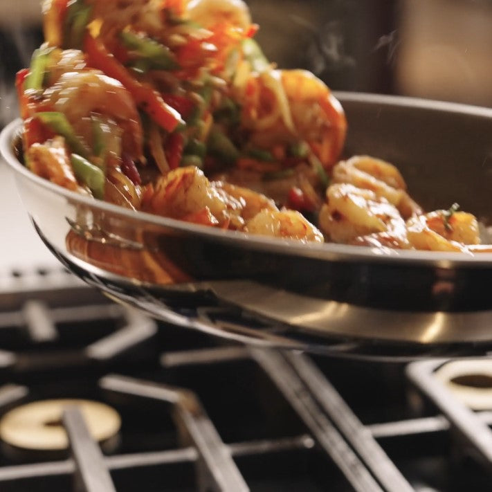 Shrimp and colorful veggies sizzle in the Viking PureGlide Pro 3-Ply 10 Inch Fry Pan by Viking Culinary Products, steam rising as they're tossed over the stovetop for healthy cooking.