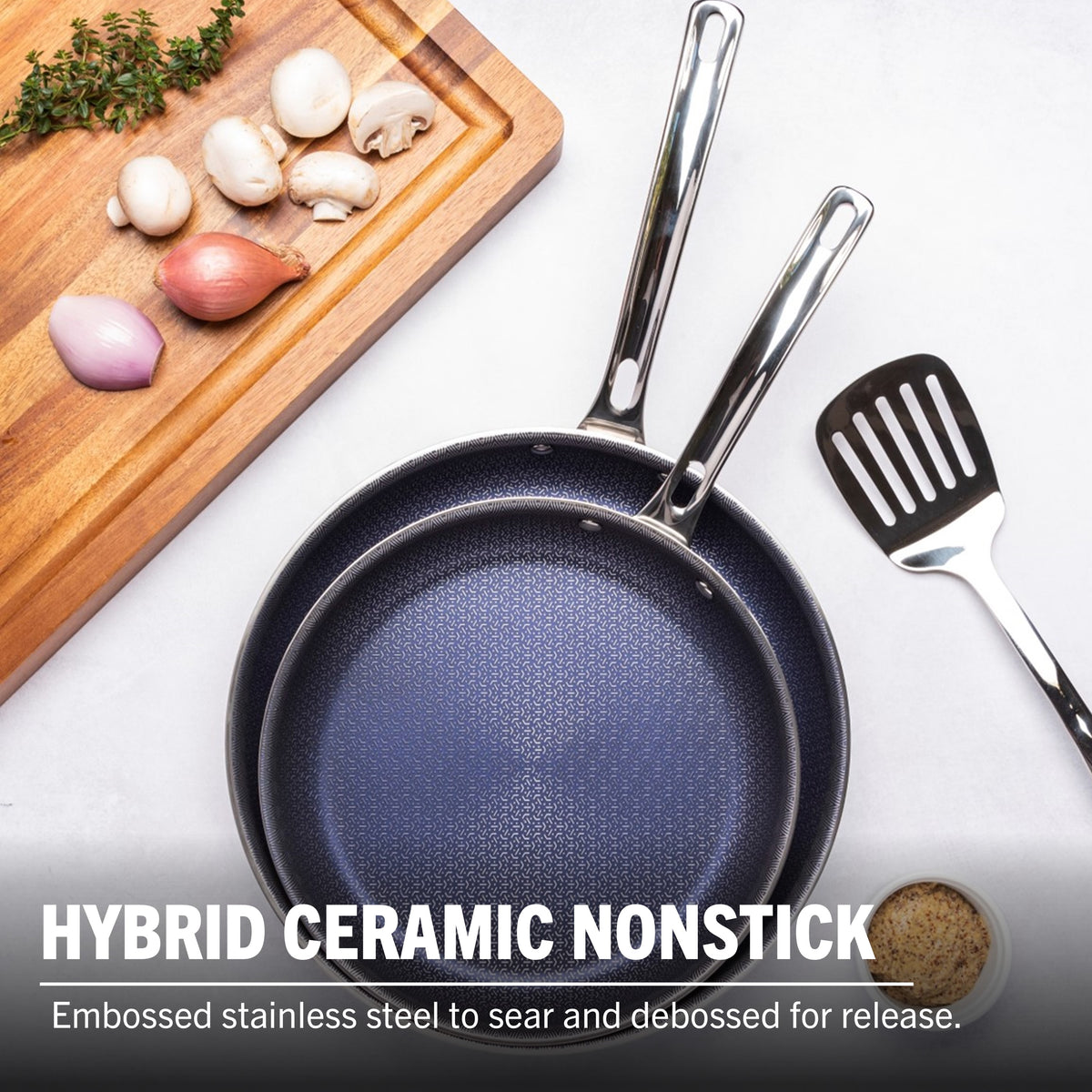 The Viking 3-Ply Hybrid Plus Ceramic 2 Pc Nonstick Fry Pan Set by Viking Culinary Products (9.5" & 11", metal handles) is shown on a white surface with a spatula, cutting board with mushrooms, shallots, garlic, and seasoning, highlighting its induction ready durability.