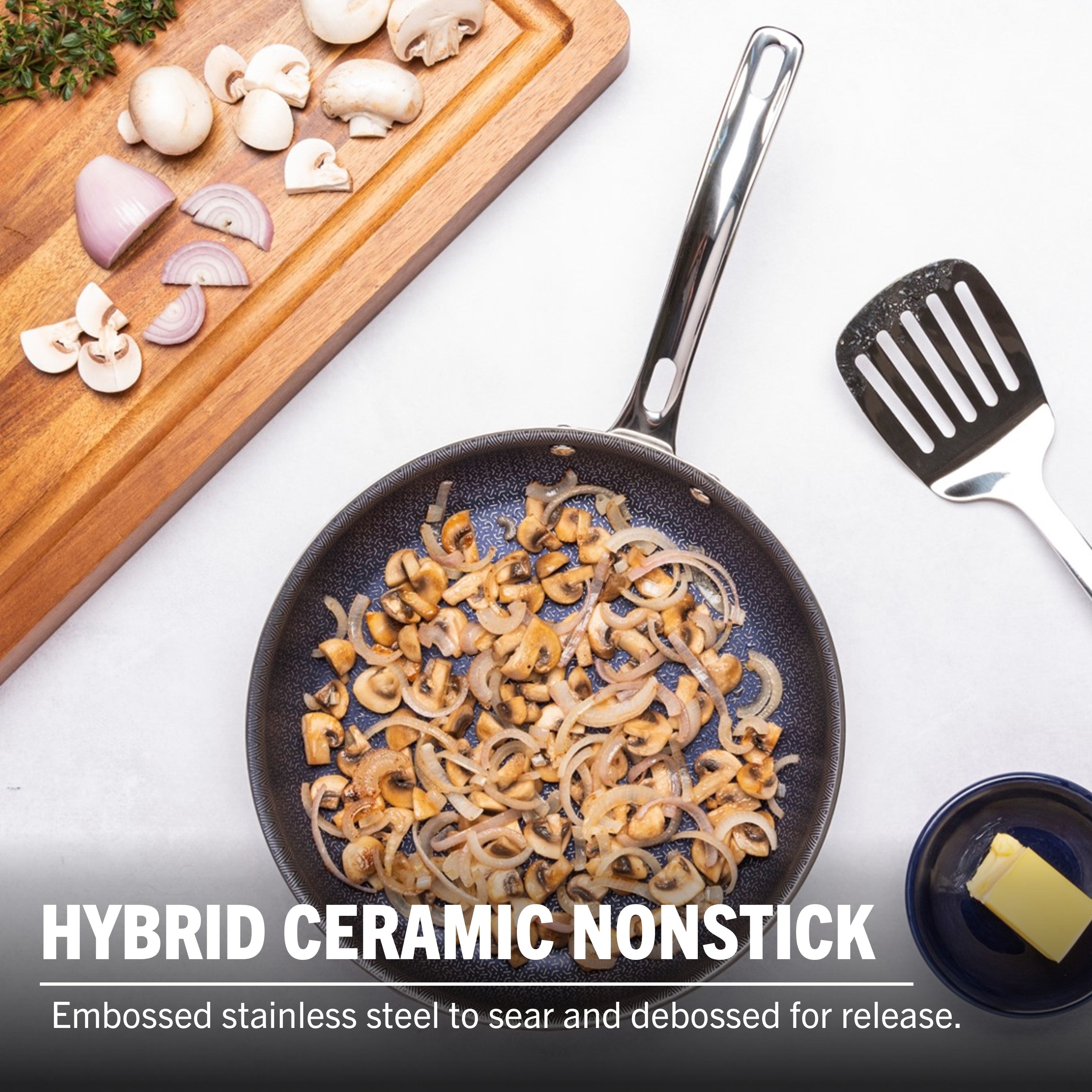 A Viking Culinary Products 3-Ply Hybrid Plus Ceramic 8-inch Nonstick Fry Pan with sautéed mushrooms and onions sits on a white surface, near a spatula, butter dish, and cutting board with chopped mushrooms, shallots, and herbs. Induction capable.