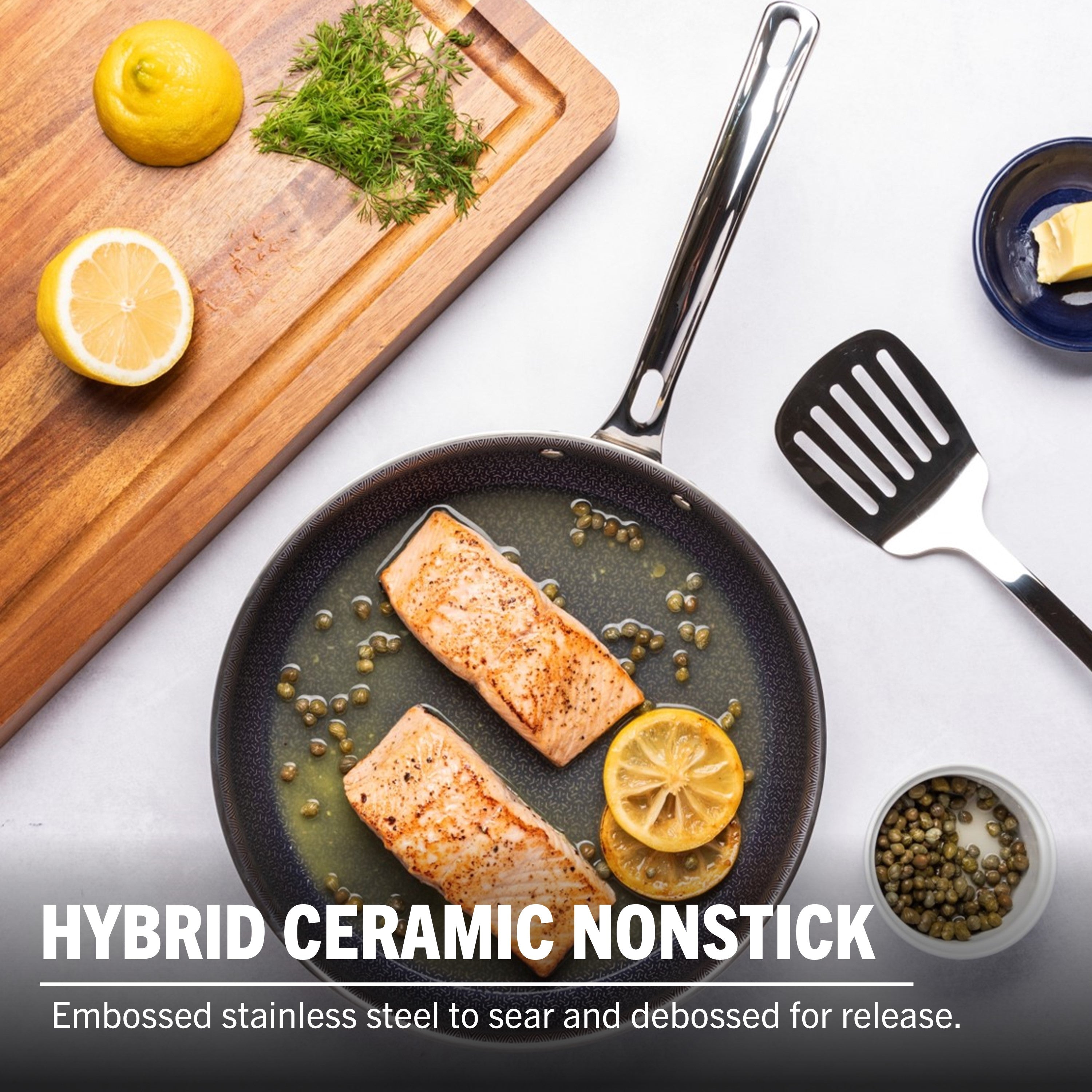 The Viking 3-Ply Hybrid Plus Ceramic 10-inch Nonstick Fry Pan by Viking Culinary Products sits on a counter with salmon fillets, lemon slices, and capers. Nearby are a spatula, butter, lemon half, and fresh dill.
