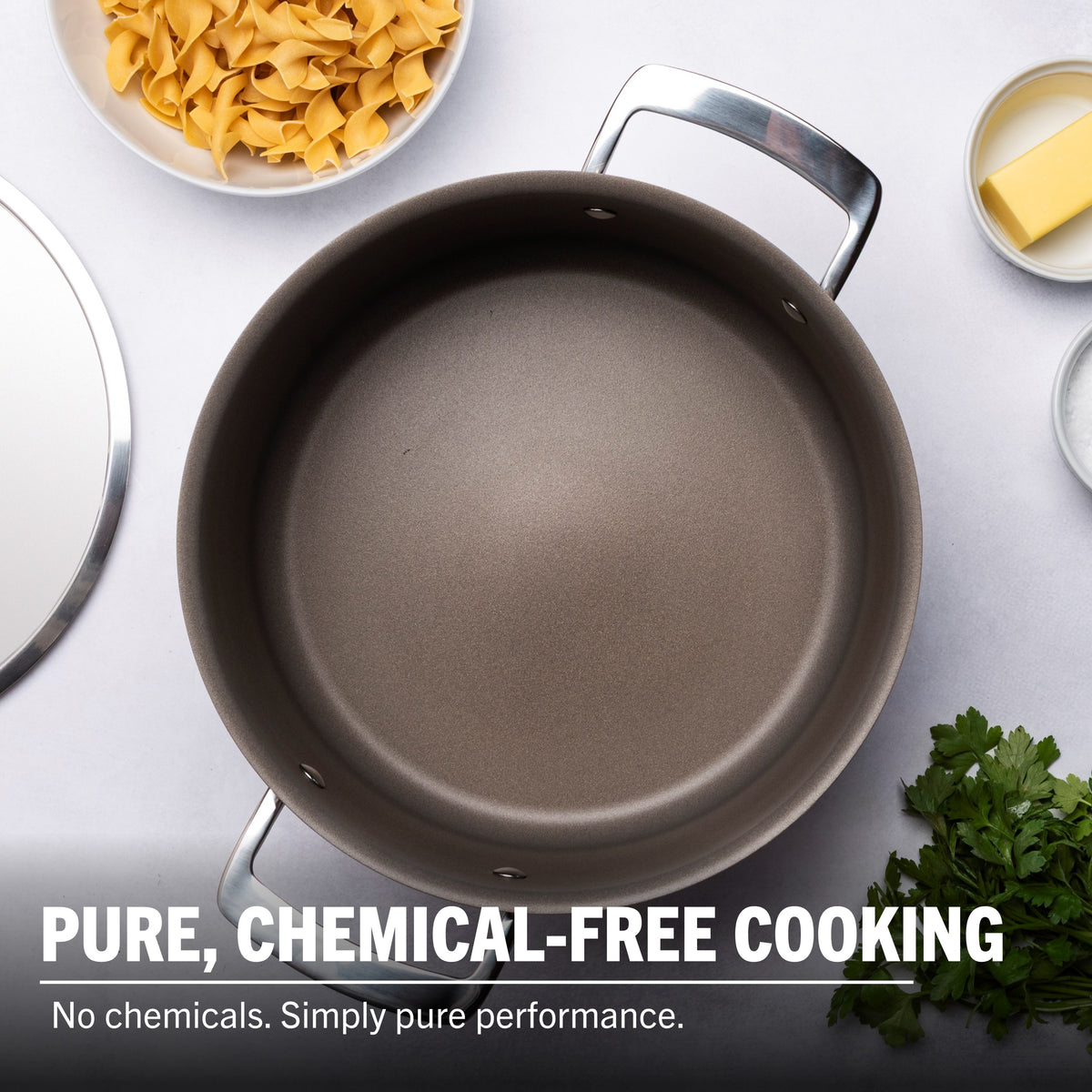 A spotless Viking PureGlide Pro 3-Ply 6-Quart Dutch Oven with Metal Lid by Viking Culinary Products rests on a white surface, surrounded by dry pasta, butter, parsley, and a lid. Text: PURE, CHEMICAL-FREE COOKING. No chemicals. Simply pure performance.