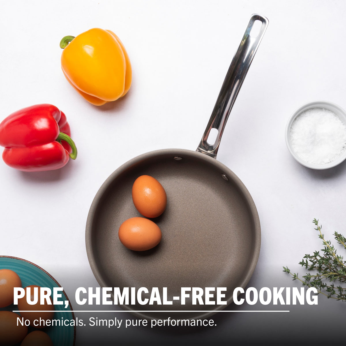 A Viking Culinary Products PureGlide Pro 3-Ply 8 Inch Fry Pan with two eggs sits on a white surface, surrounded by yellow and red bell peppers, a bowl of salt, blue plate, and thyme. Text reads: Pure cooking. No chemicals—just healthy performance.