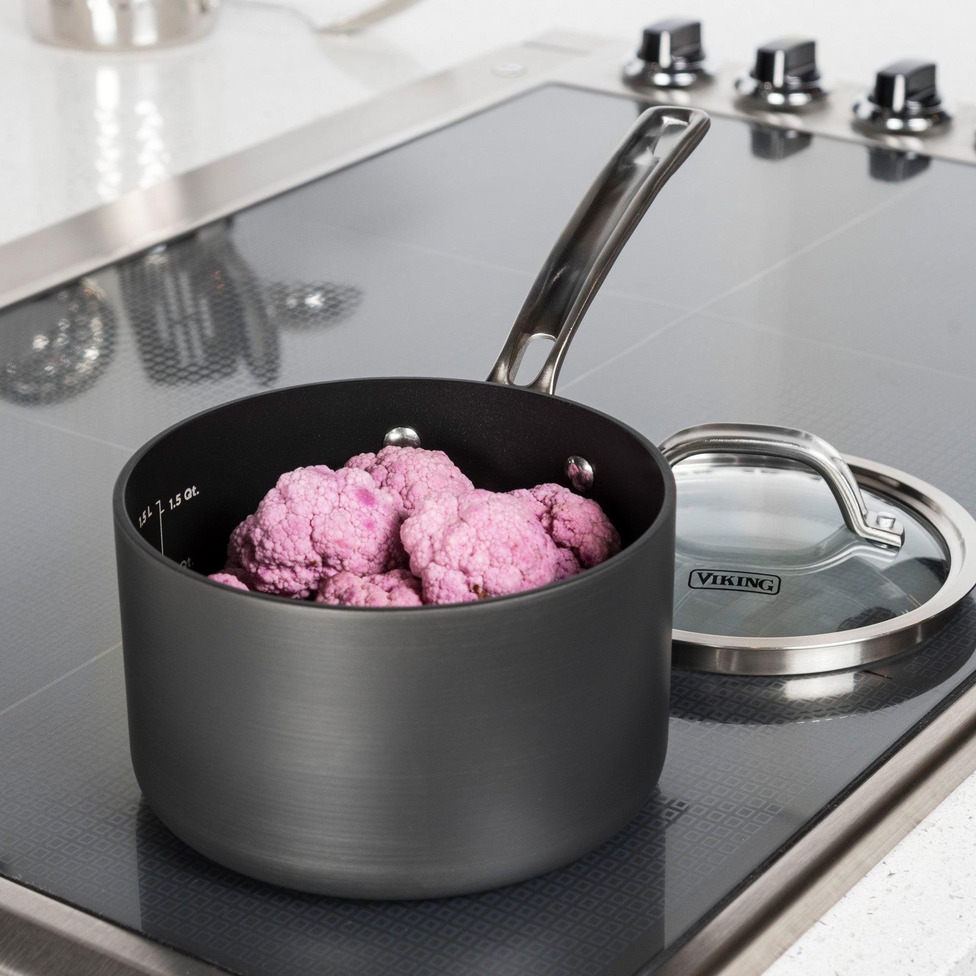 The Viking Culinary Products Hard Anodized Nonstick 2-Quart Sauce Pan with Glass Lid holds vibrant purple cauliflower florets on a modern stovetop, its sturdy metal handle beside the tempered glass lid.