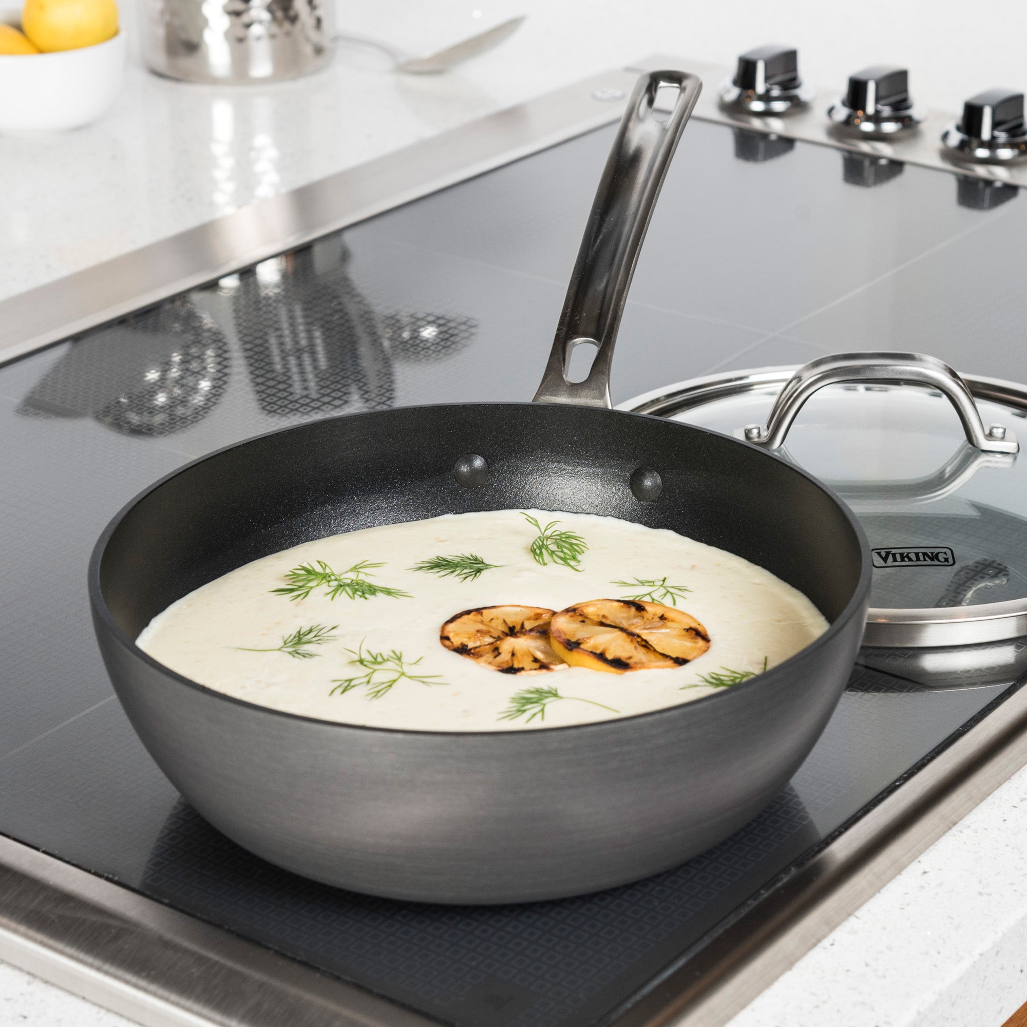 A Viking Hard Anodized Nonstick 3-Quart Saucier Pan by Viking Culinary Products, filled with creamy soup and topped with grilled mushrooms and dill, sits on a stove with its glass lid next to it.