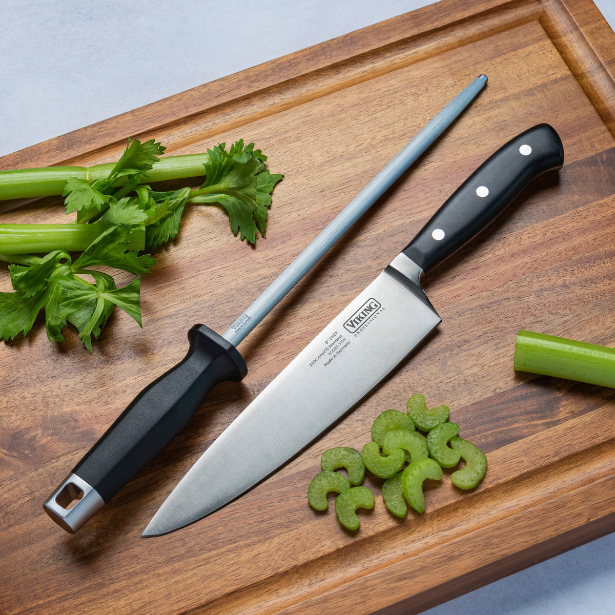 The Viking Professional 8-Inch Chefs Knife by Viking Culinary Products and a honing rod rest on a wooden cutting board with celery stalks and sliced pieces, demonstrating excellent edge retention for precision cuts.