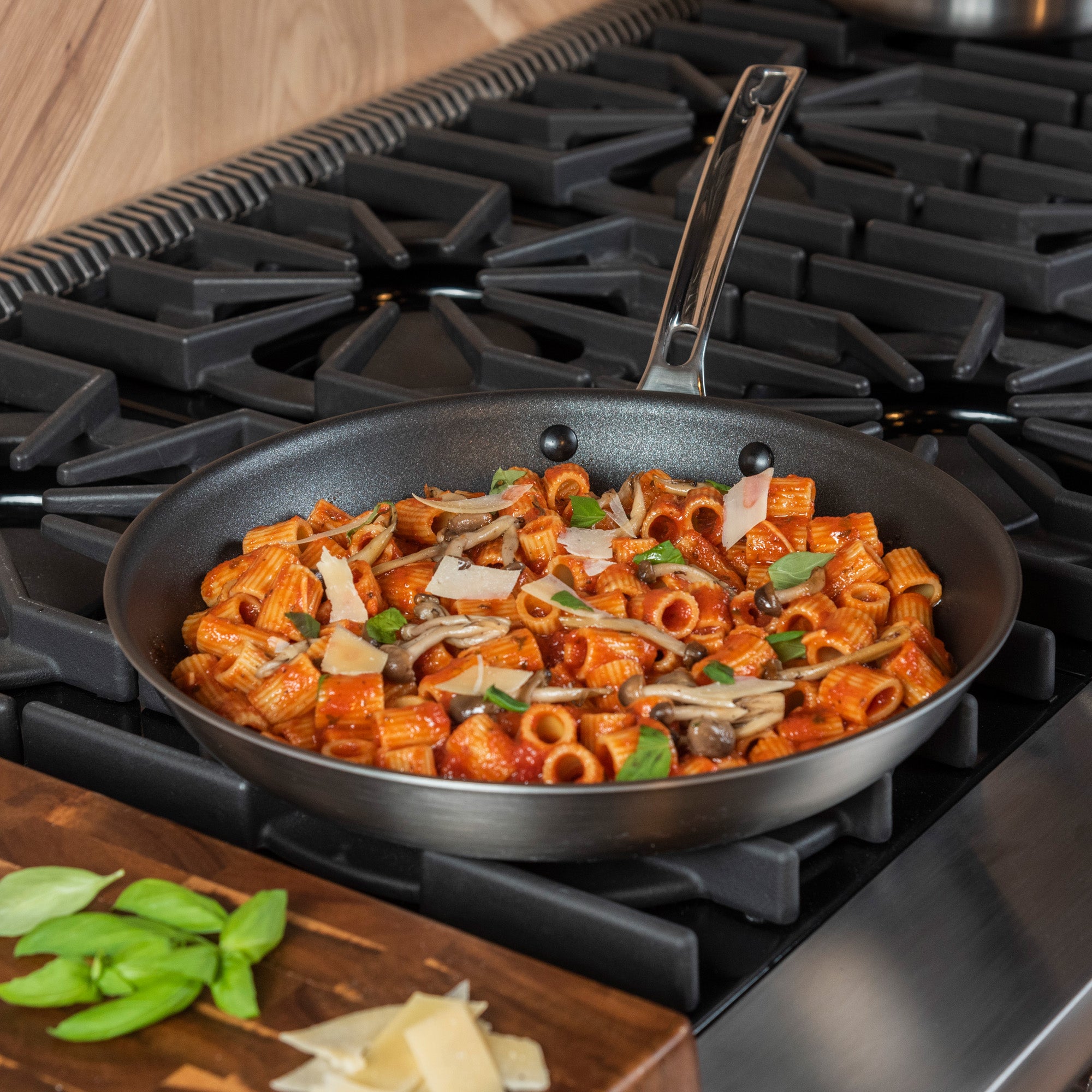 The Viking Professional 5-Ply 12-Inch Nonstick Fry Pan by Viking Culinary Products, featuring a stainless steel interior and Stay-Cool Handles, sits on the stovetop filled with rigatoni in tomato sauce, basil, parmesan shavings, and mushrooms.