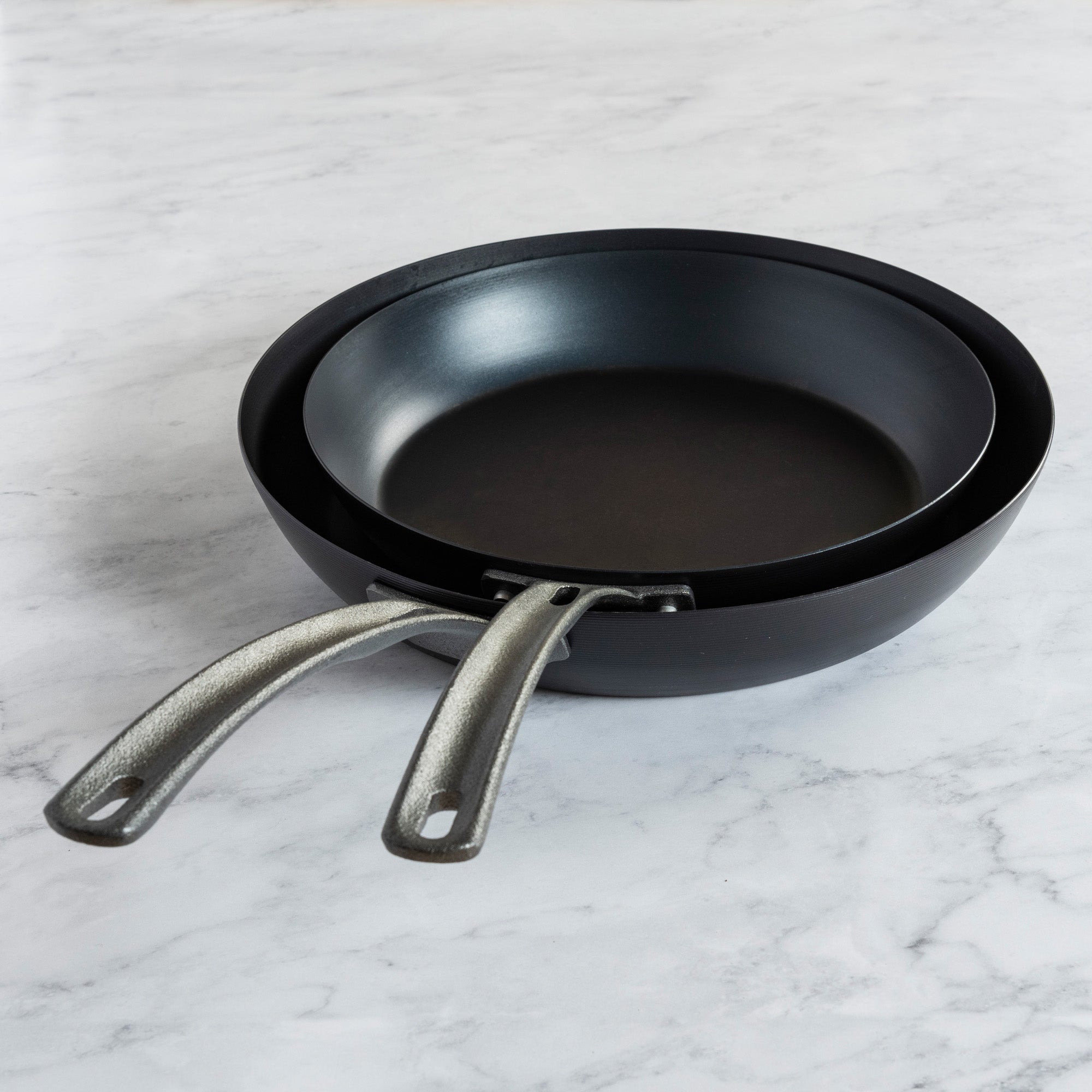 The Viking Culinary Products 2-Piece Blue Carbon Steel Fry Pan Set features two pre-seasoned fry pans with metal handles, nested together on a white marble surface—durable, lightweight cookware ideal for daily cooking.