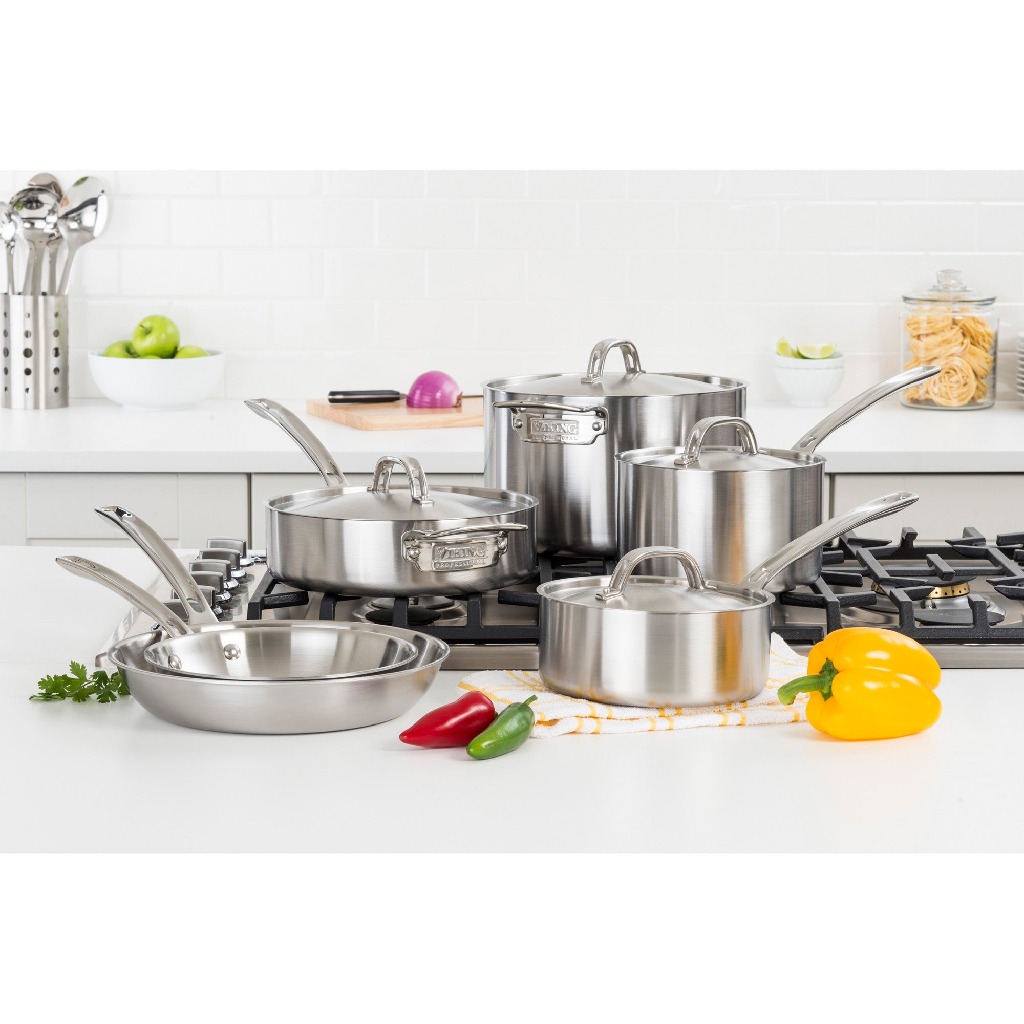 The Viking Culinary Products Professional 5-Ply 10-piece Cookware Set is displayed on a white kitchen counter, featuring frying pans, saucepans, and a stockpot with lids, surrounded by colorful peppers and fresh ingredients.