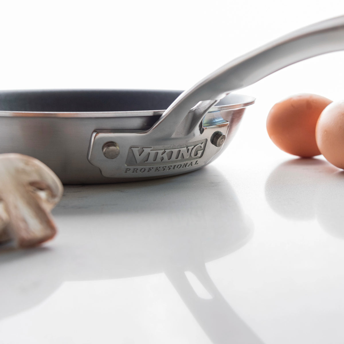 A stainless steel Viking Professional frying pan on a white surface, with eggs and mushrooms nearby.