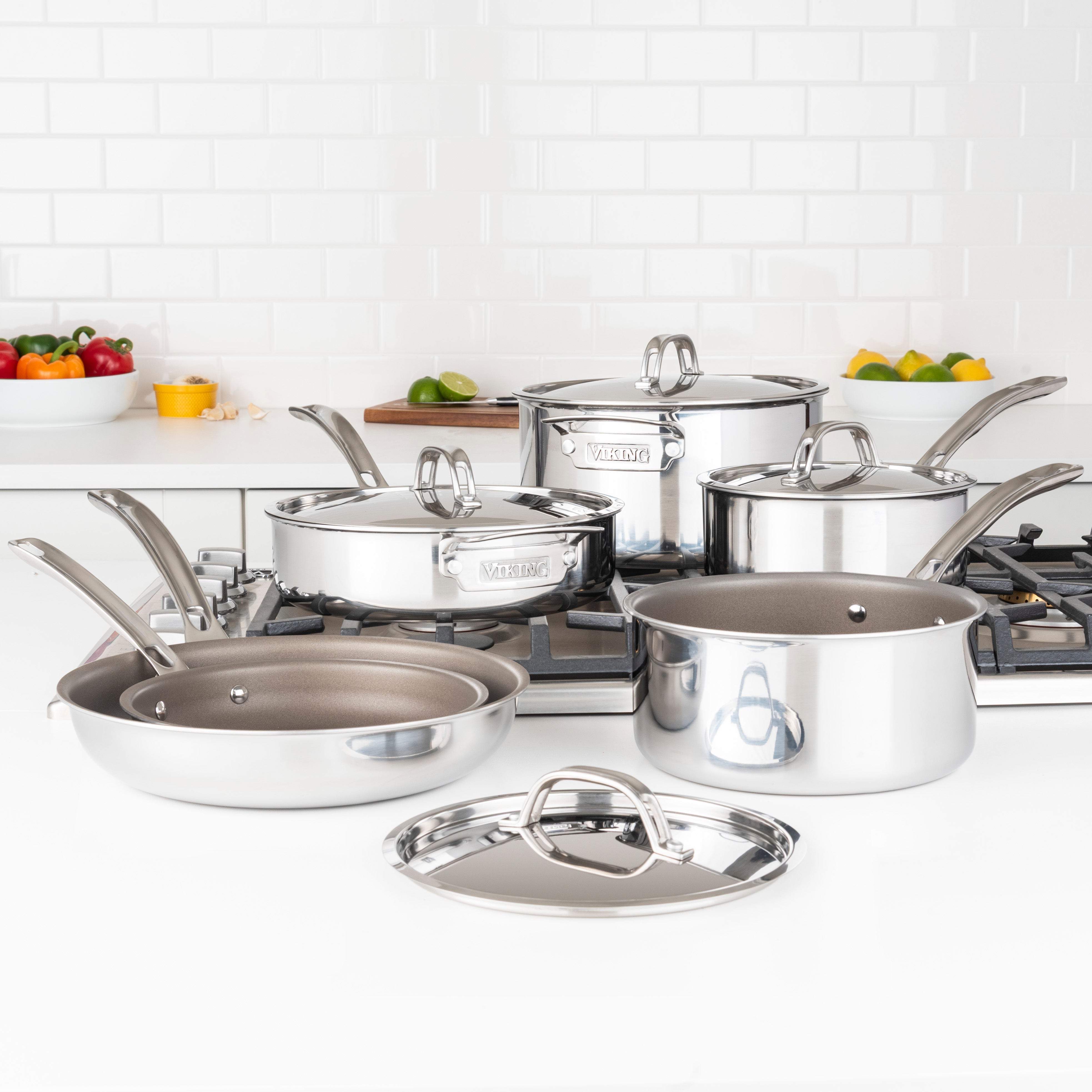 The Viking Culinary Products PureGlide Pro 3-Ply 10-Piece Cookware Set is displayed on a white kitchen countertop near a stove, accompanied by fresh vegetables and citrus fruit.