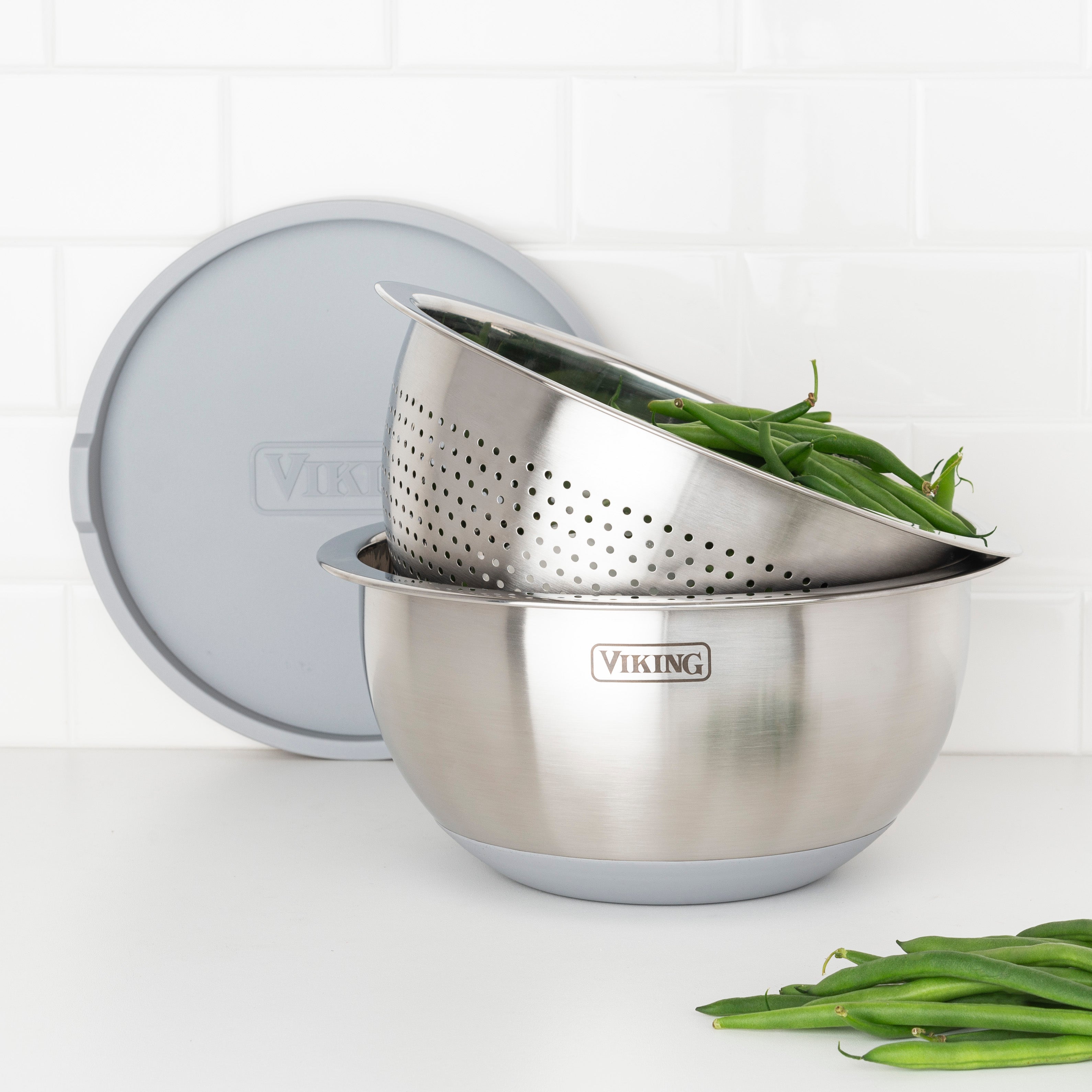The Viking Culinary Products 9-Piece Stainless Steel Mixing Bowl Set with Strainer, Gray, is shown on a white surface with green beans inside and features a silicone base and gray lid.