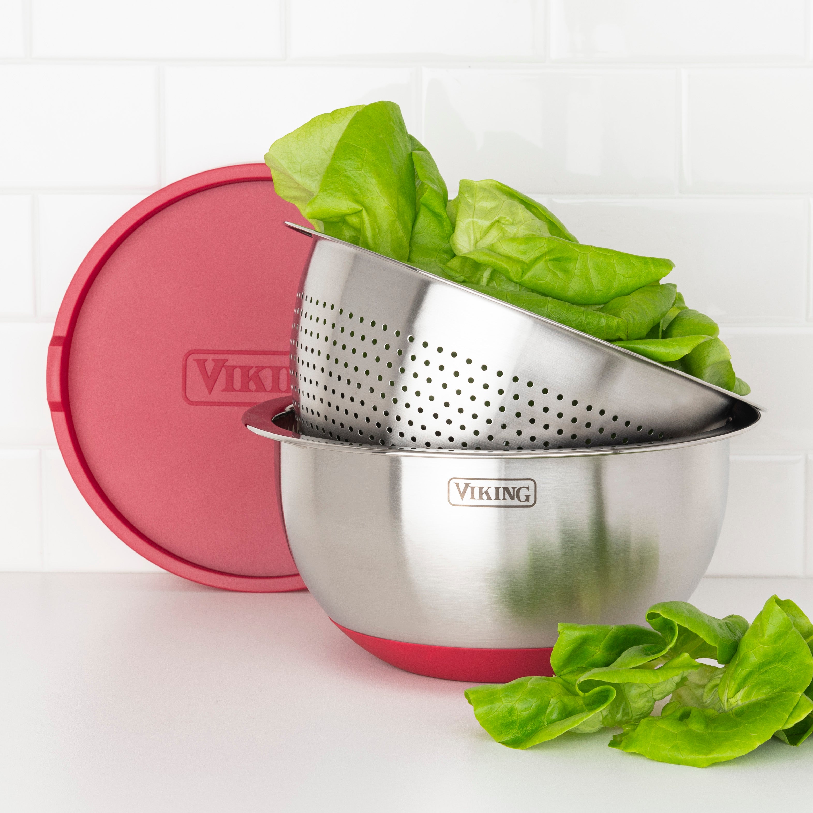 The Viking 9-Piece Stainless Steel Mixing Bowl Set with Strainer by Viking Culinary Products includes bowls with airtight lids for freshness and a bowl that doubles as a colander, shown with crisp lettuce inside and beside it on a white surface.