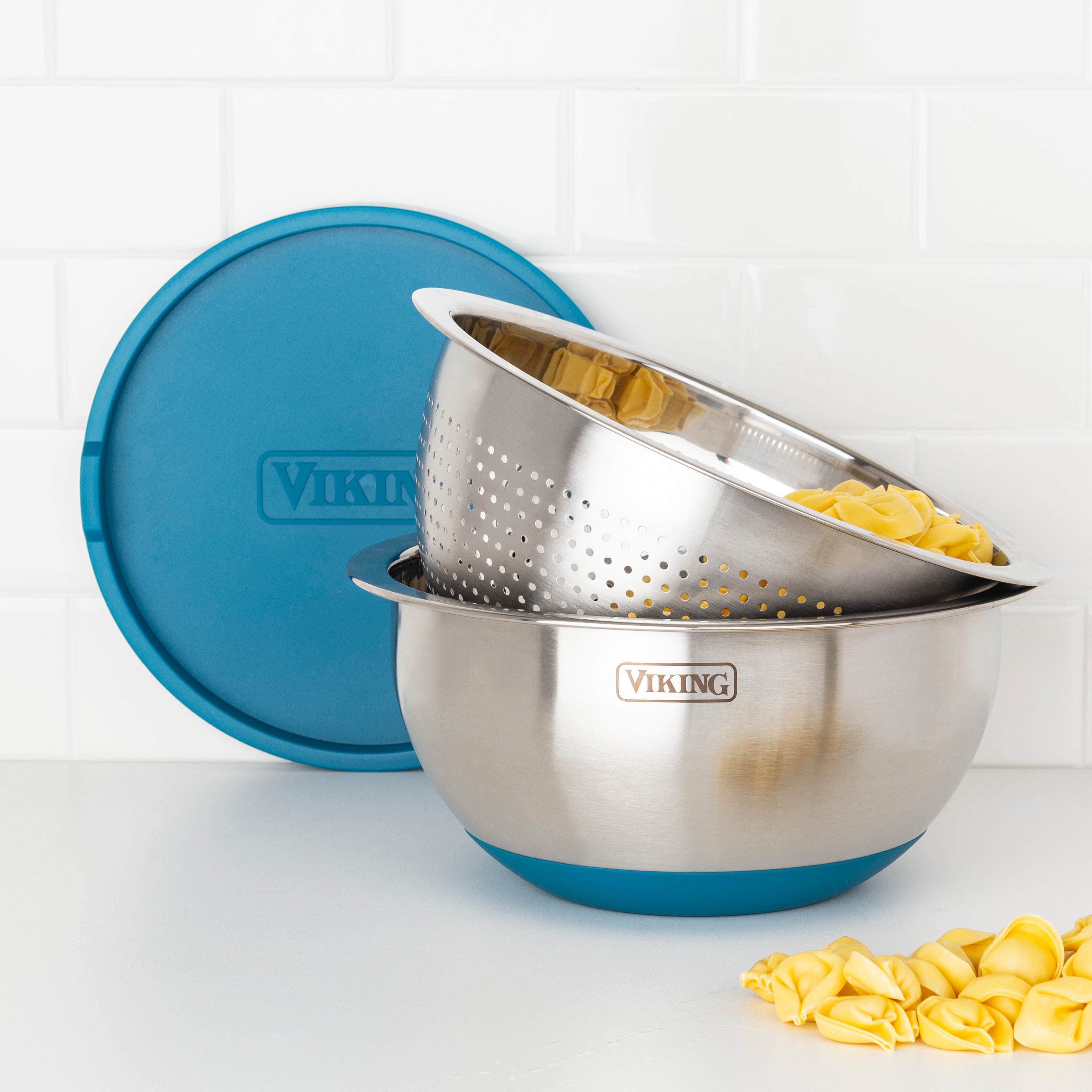 The Viking Culinary Products 9-Piece Stainless Steel Mixing Bowl Set with Strainer in teal features non-slip bases and an airtight lid, offering compact storage. Perfect for displaying uncooked pasta in the strainer on your countertop.
