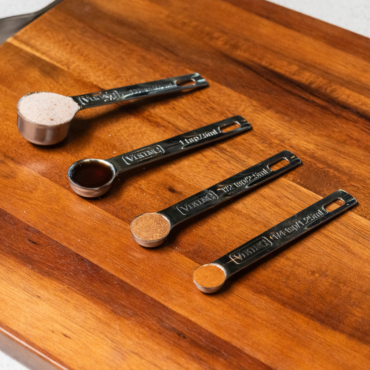 The Viking 4pc Stainless Steel Measuring Spoon Set by Viking Culinary Products features four nesting spoons, ideal for measuring salt, liquids, or spices, and keeps your kitchen organized and storage simple on any cutting board.