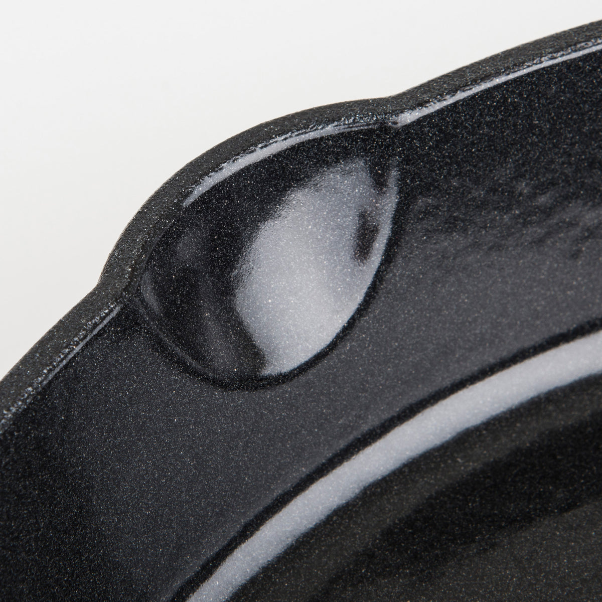 Close-up of the lip and pouring spout of a black, speckled enamel-coated cast iron skillet against a white background.
