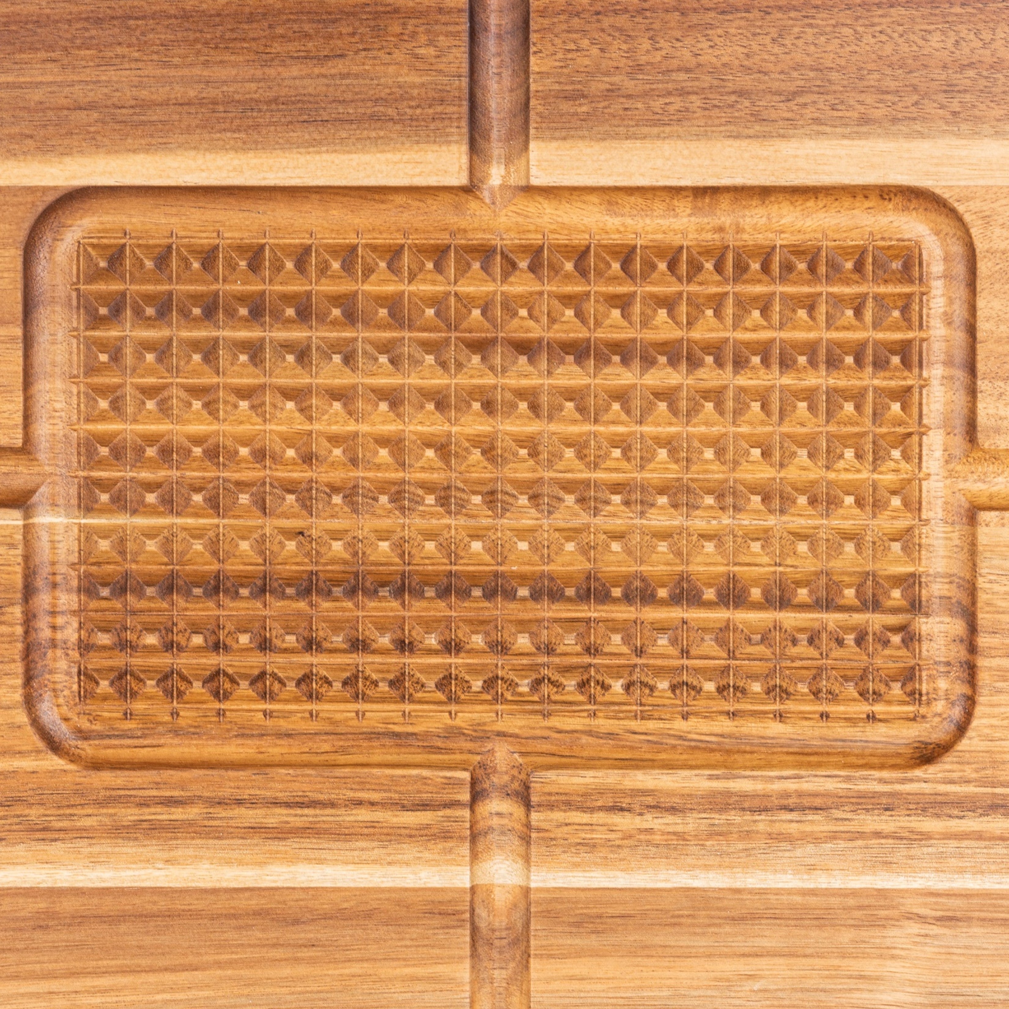 A close-up of a wooden cutting board with a textured, diamond-patterned section in the center and grooved edges. The wood has a polished finish with visible grain.
