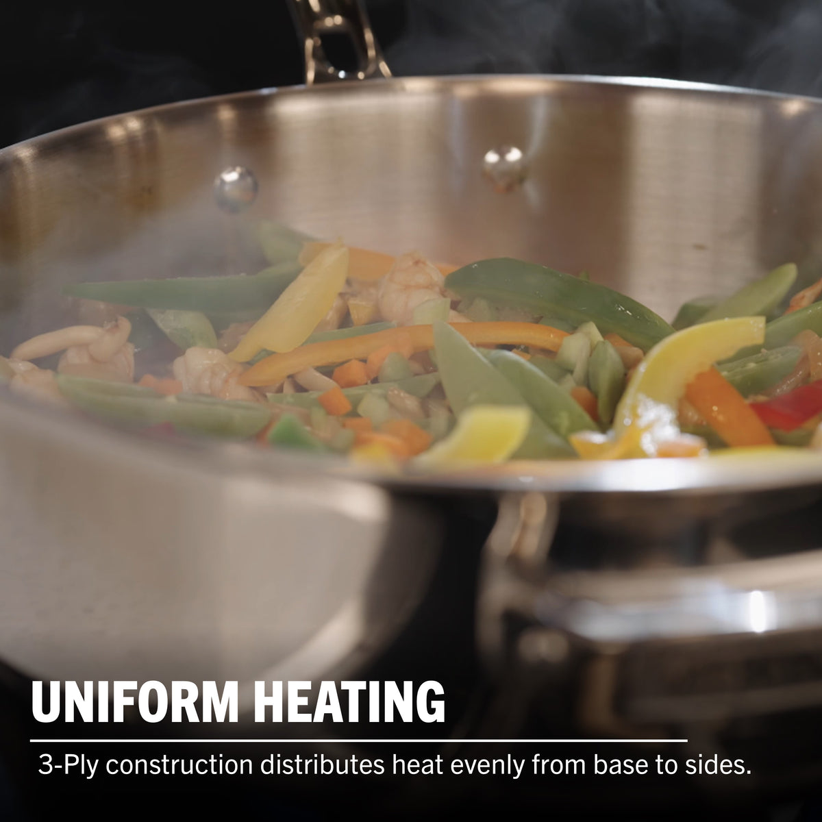 A Viking Artisan 3-ply Stainless Steel 11-Piece Cookware Set with Glass Lids by Viking Culinary Products sautés colorful veggies, emitting steam. Text reads: UNIFORM HEATING. 3-ply construction ensures even heat from base to sides and is induction compatible.