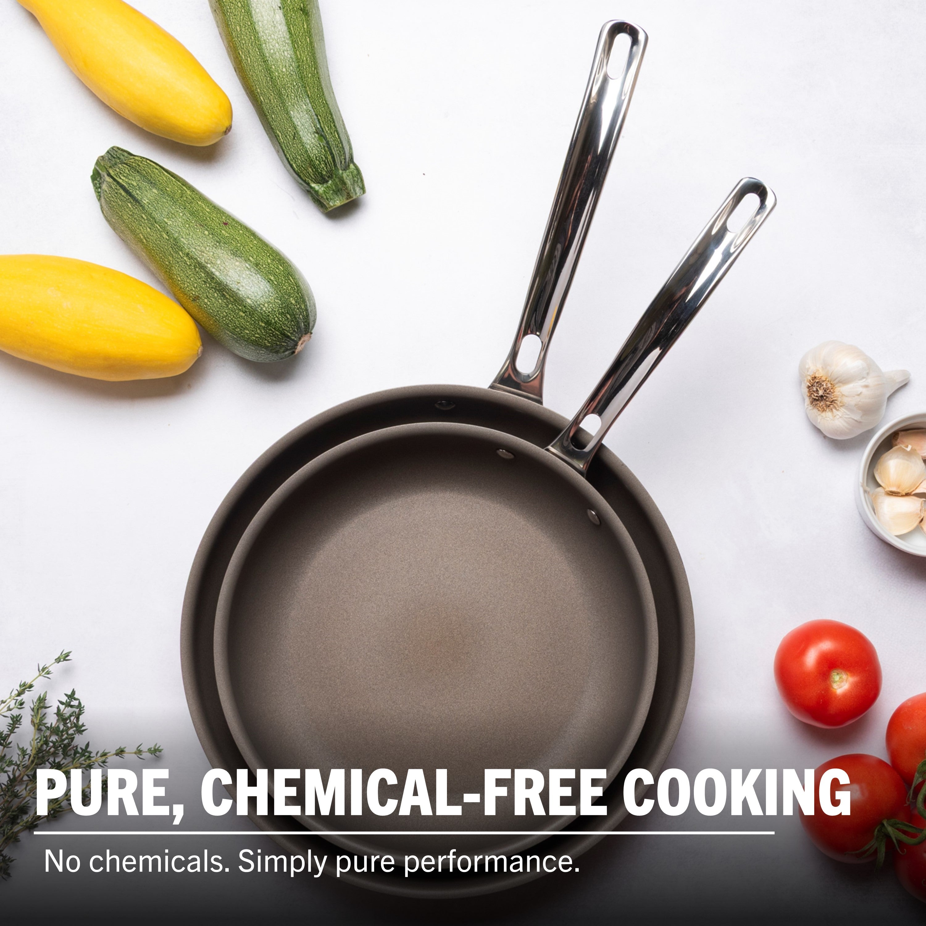 The Viking Culinary Products PureGlide Pro 3-Ply 2-Piece Fry Pan Set (9.5" & 11") with metal handles rests on a white surface amid fresh veggies and herbs—ideal for healthy cooking. Text: PURE, CHEMICAL-FREE COOKING.