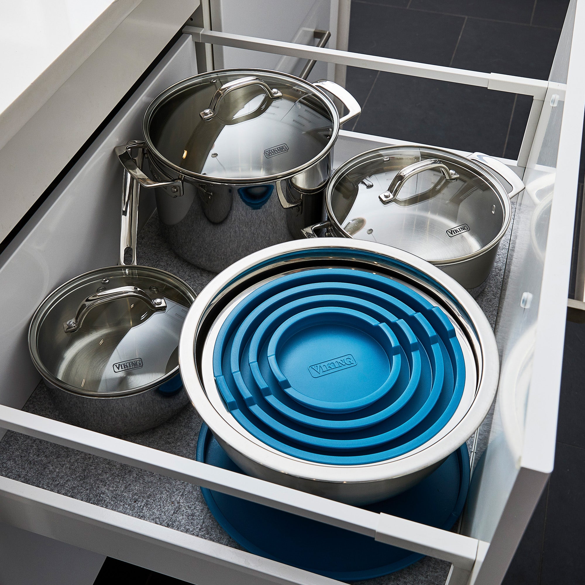 Open kitchen drawer with three stainless steel pots and lids, plus a Viking 10-Piece Stainless Steel Mixing Bowl Set with teal lids by Viking Culinary Products, all nested for compact storage on a grey-lined drawer.
