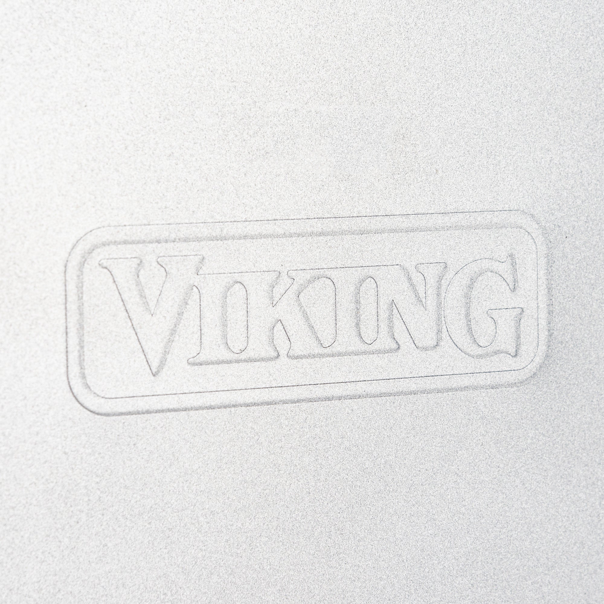 Close-up of the word VIKING embossed in a rectangle on a metallic, light gray surface, highlighting the Viking 15-Inch Aluminized Nonstick Baking Sheet from Viking Culinary Products, crafted from durable aluminized steel.