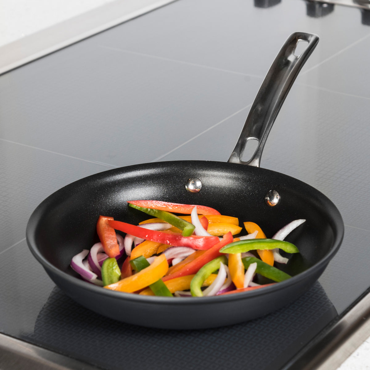 A Viking Hard Anodized Nonstick 8-inch Fry Pan by Viking Culinary Products sits on a stovetop, sizzling with sliced red, yellow, and green bell peppers mixed with red onions on its nonstick surface.