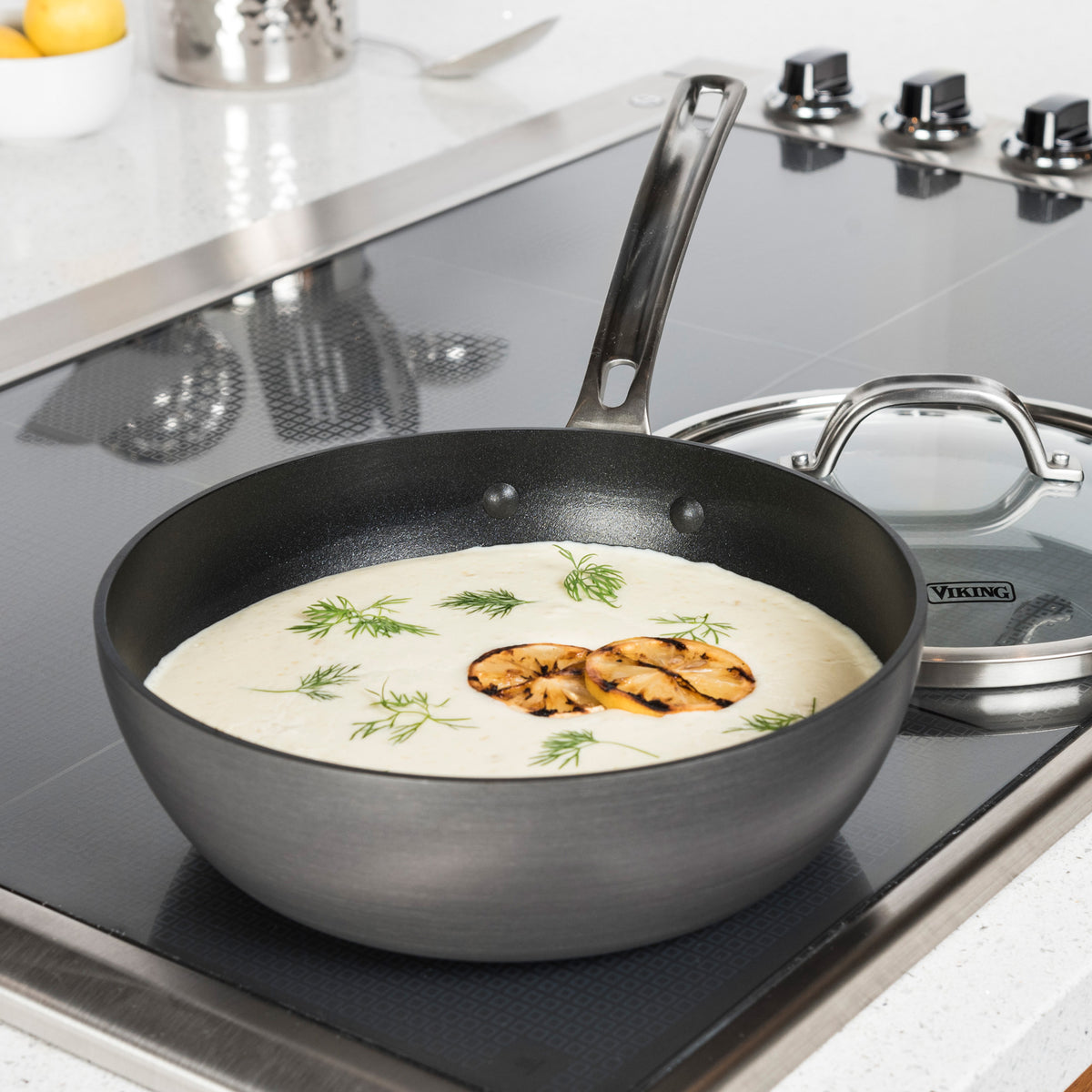 A Viking Hard Anodized Nonstick 3-Quart Saucier Pan by Viking Culinary Products, filled with creamy soup and topped with grilled mushrooms and dill, sits on a stove with its glass lid next to it.