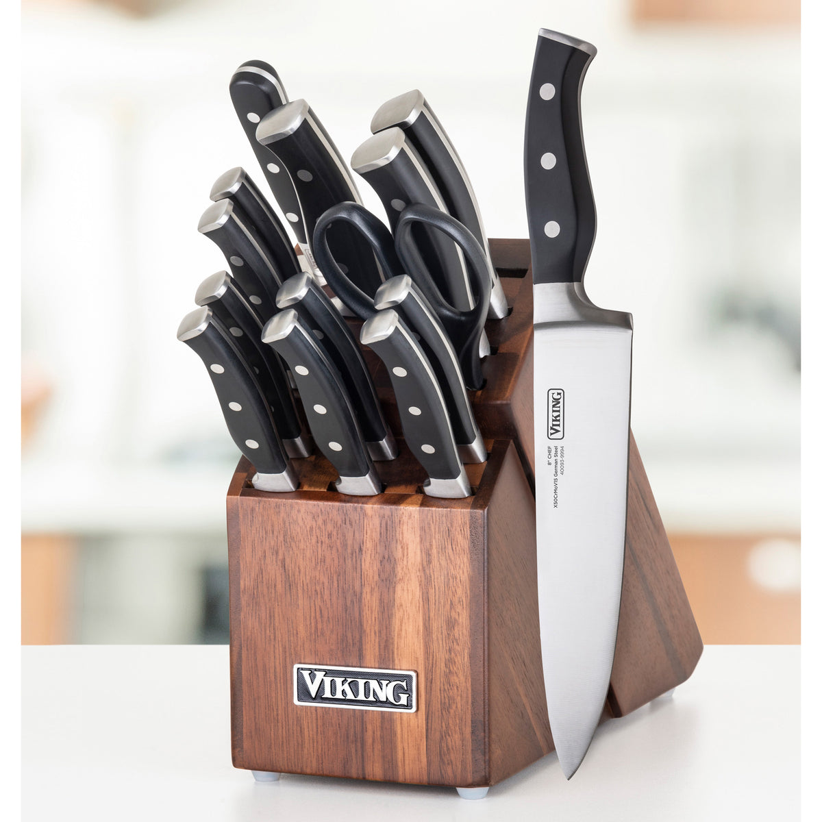 The Viking Professional 15-Piece Stainless Steel Cutlery Set by Viking Culinary Products features black-handled knives, including a German stainless steel chef’s knife and kitchen scissors, in an acacia wood block on a white countertop.