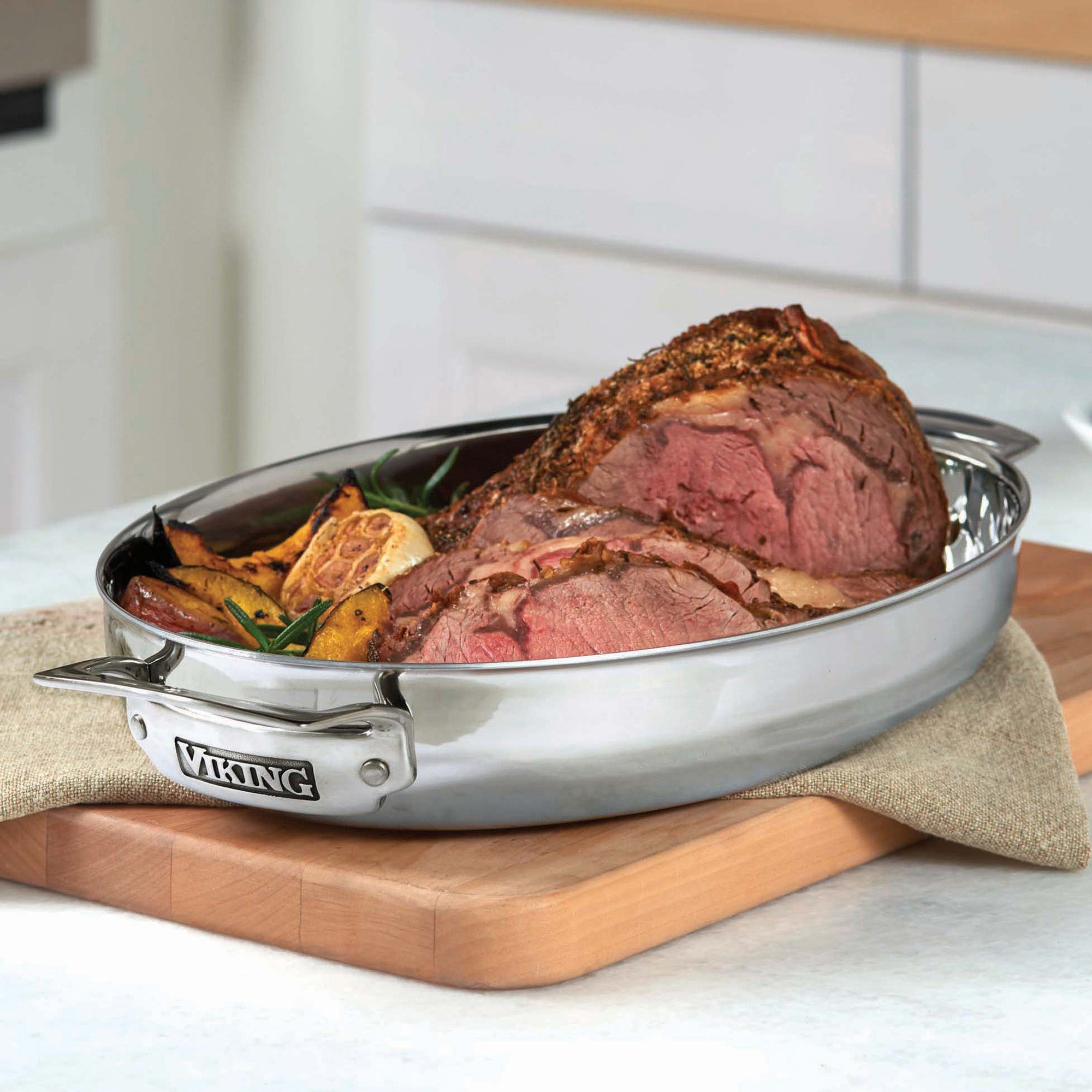 The Viking 3-Ply 8.5-Quart 3-in-1 Oval Roaster with Rack by Viking Culinary Products holds a cooked roast and vegetables, with its induction lid, resting on a wooden cutting board in the kitchen.