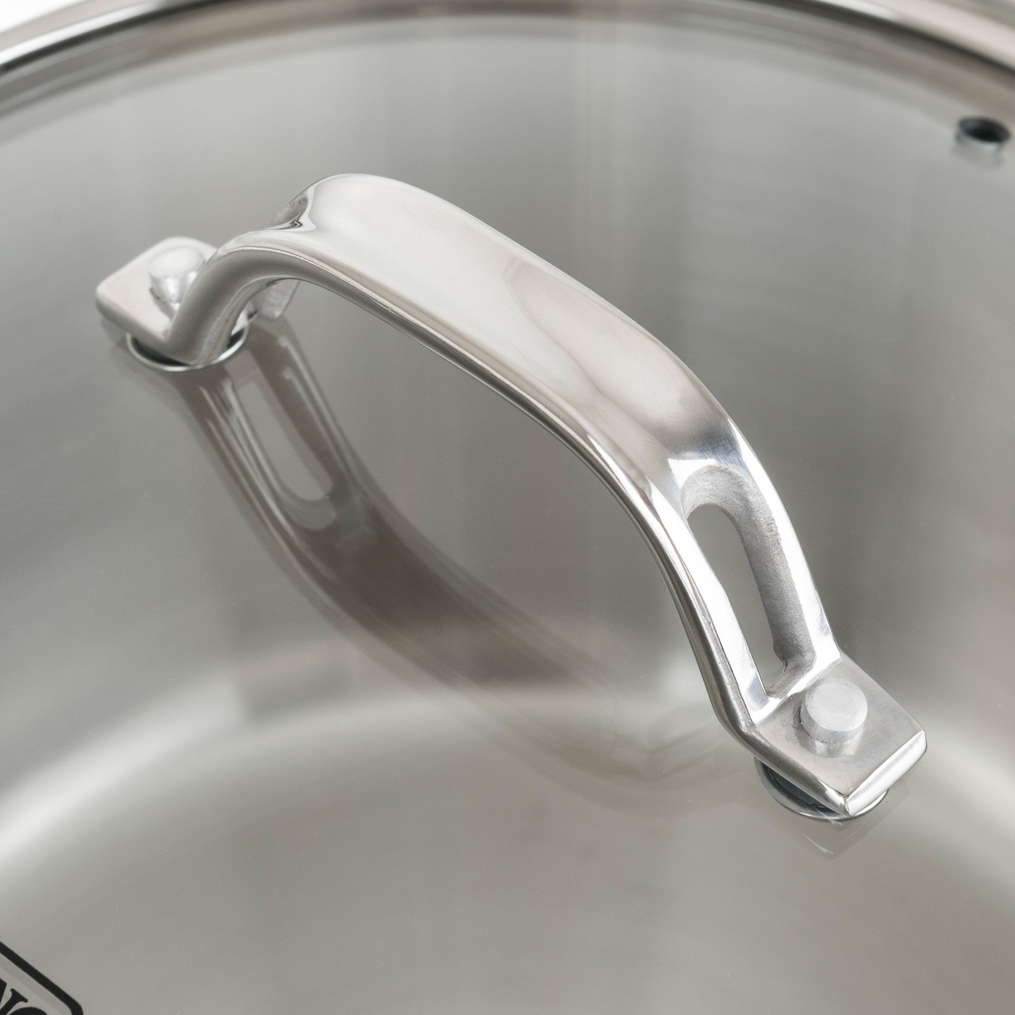 Close-up of a polished stainless steel handle on the glass lid of a Viking Contemporary 3-Ply Stainless Steel Cookware Set by Viking Culinary Products, showing a clear reflection on the lid.
